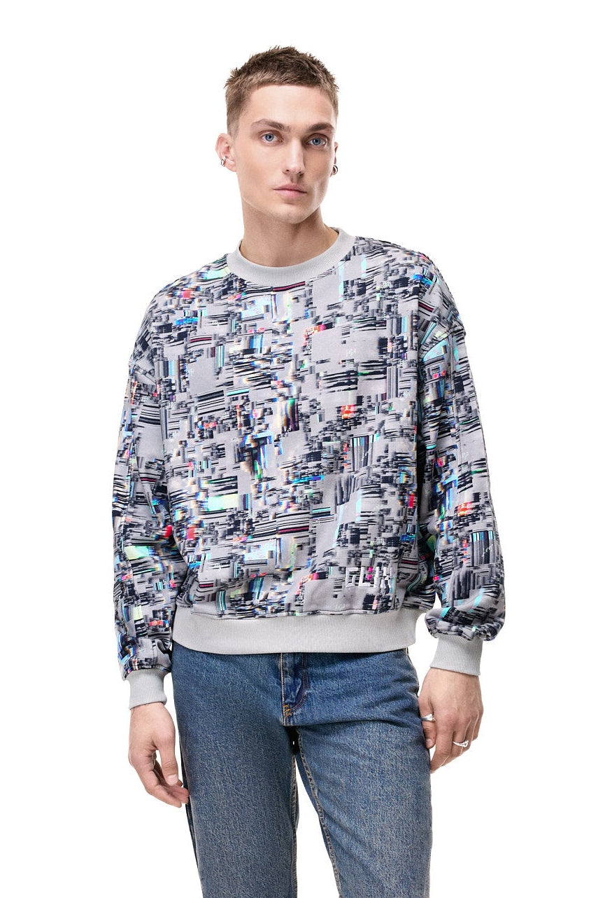 Front view of a male model wearing the GLIX "Colors' Echo" grey oversized sweatshirt, showcasing the intricate all-over multicolor digital glitch and pixelated print with a thick ribbed grey crew neckline and cuffs.