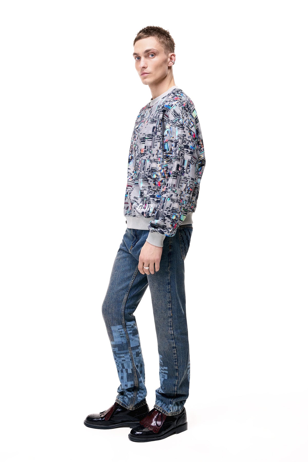 Side profile of a male model wearing the GLIX "Colors' Echo" oversized sweatshirt, highlighting the seamless continuation of the multicolor digital glitch print across the sleeves and the structured fit of the grey ribbed cuffs.