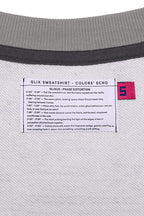 Macro close-up of the internal GLIX "Colors' Echo" white woven label featuring "GLIXUS - PHASE DISTORTION" poetic text and a pink size "S" tag, set against a grey melange sweatshirt lining.