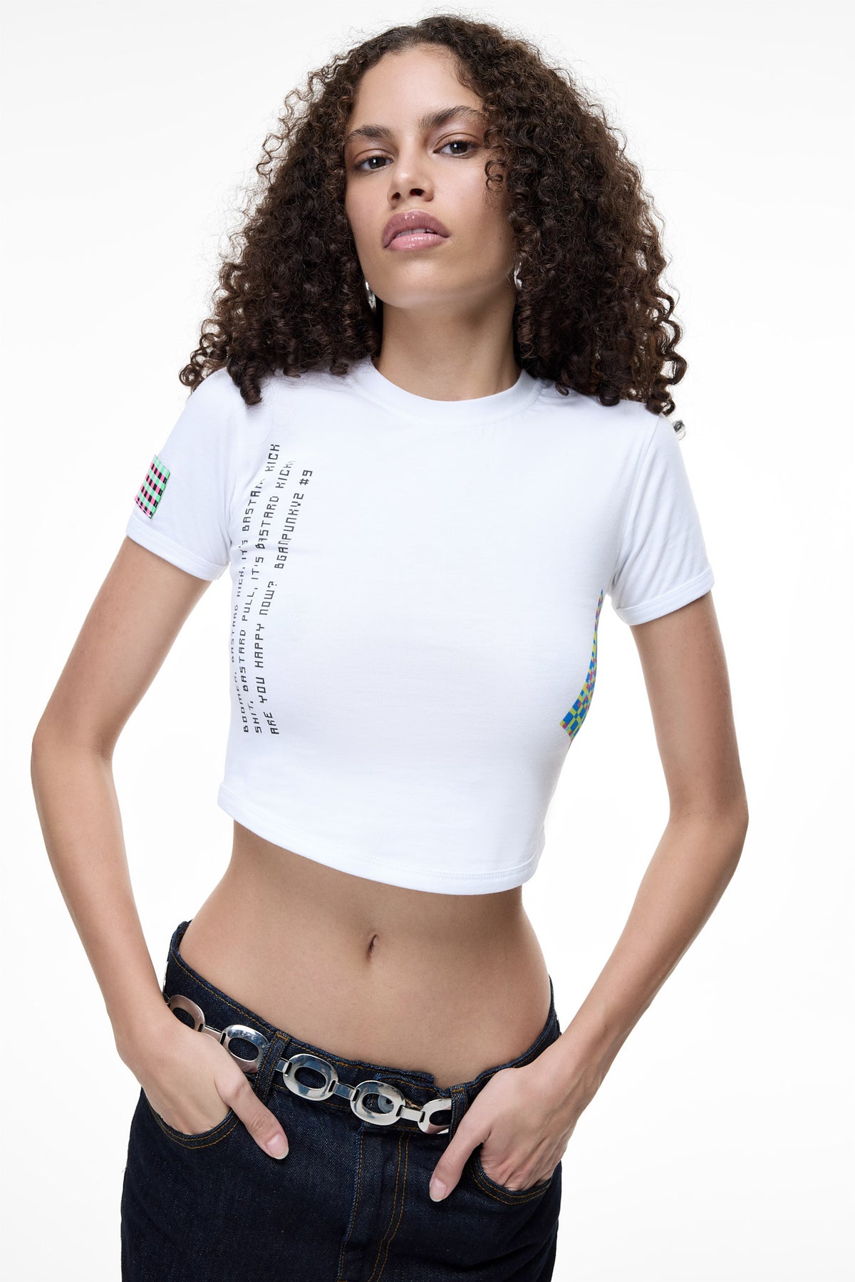 A model wearing the GLIX white crop top baby tee featuring vertical black text graphics and a colorful geometric print on the side.