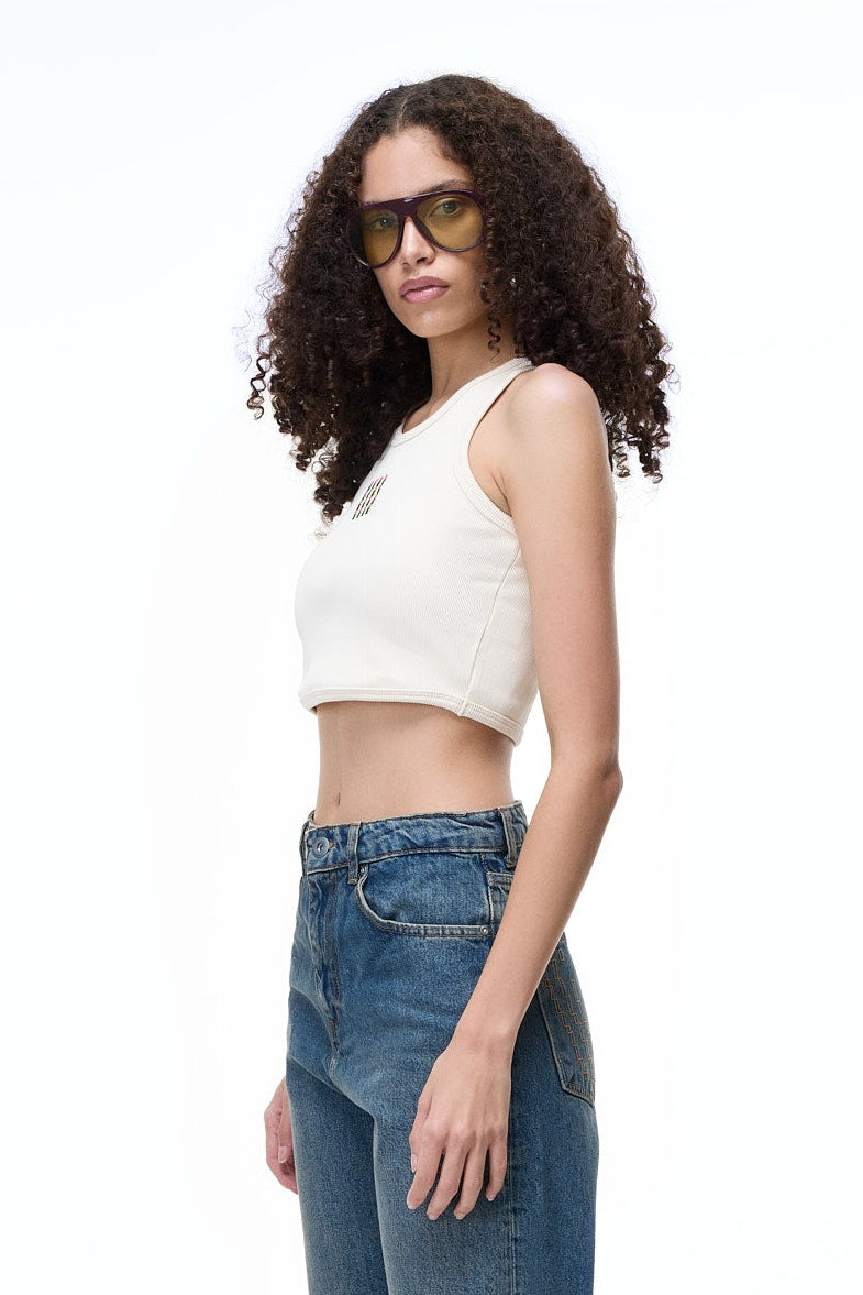 Side profile of a female model wearing the GLIX "tank.exe" white cropped tank top, paired with blue glitch-print denim jeans, showcasing the ribbed cotton texture and slim fit.