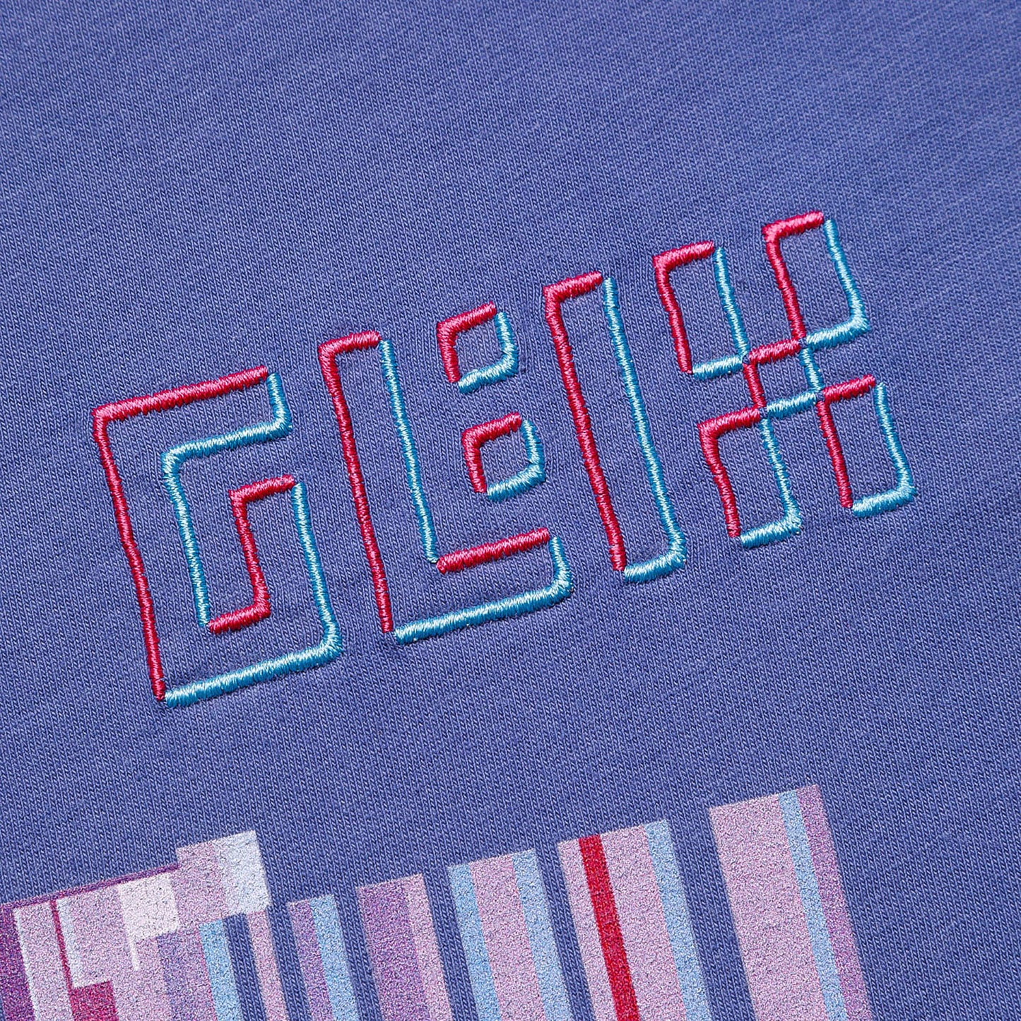 Close-up of the GLIX logo embroidered in pink and light blue on a purple crop top baby tee, featuring a pixelated graphic print below it.